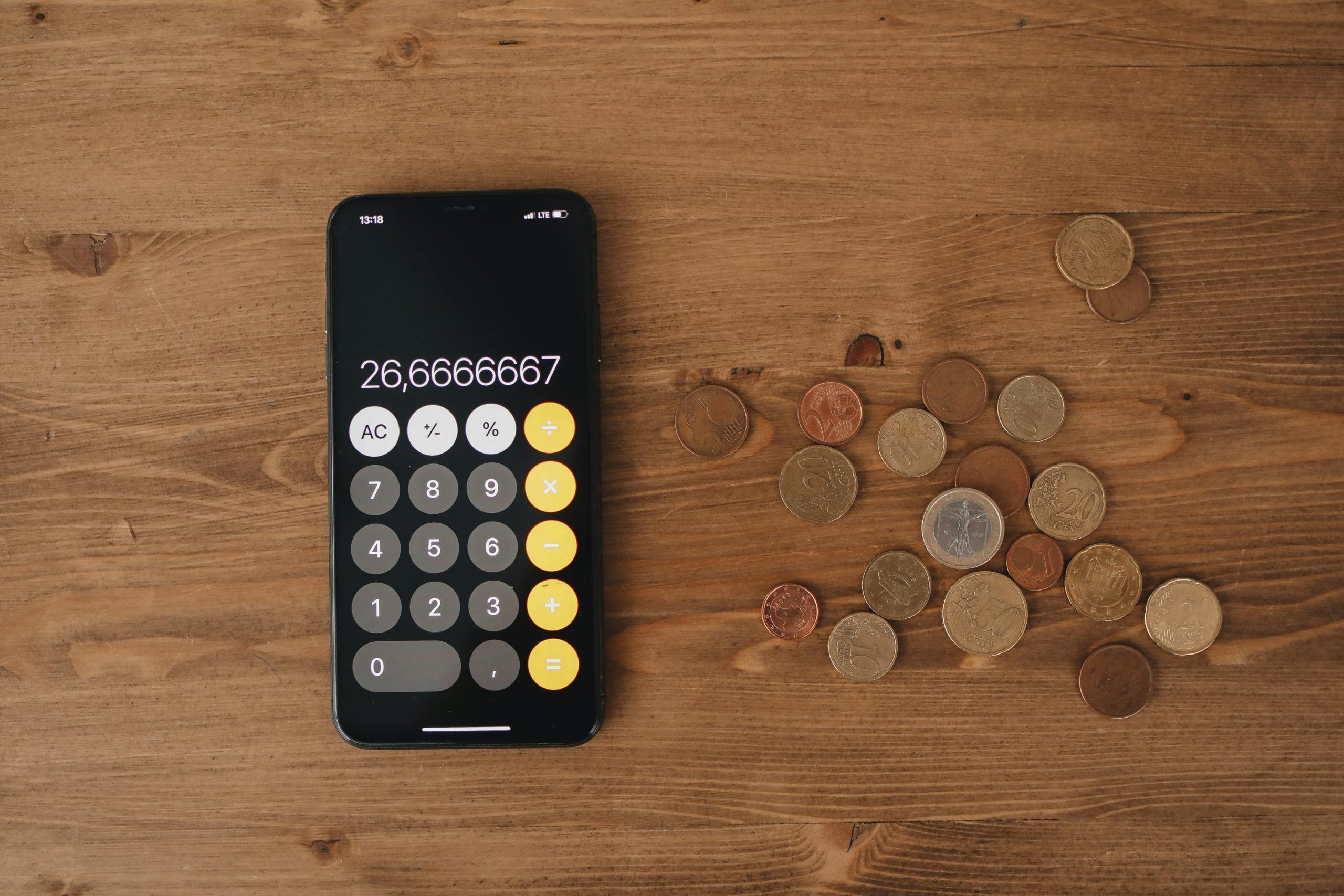 Overhead view of a smartphone calculator with European coins on a wooden surface, symbolizing modern finance.